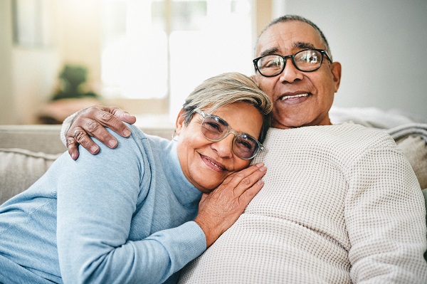 senior woman leaning on senior man while both sit on sofa at home